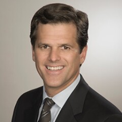Timothy Shriver smiles in a suit and tie with a short haircut