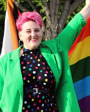 Audra Carlisle wearing a polka dot dress and holding a rainbow Pride flag