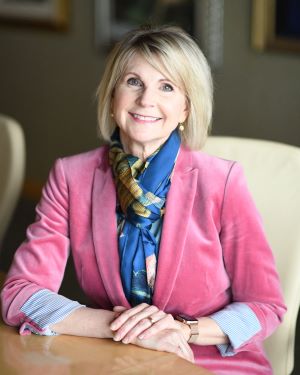 Julie L. Valentine sitting at a table in a scarf and blazer. She has straight shoulder-length hair with side-swept bangs