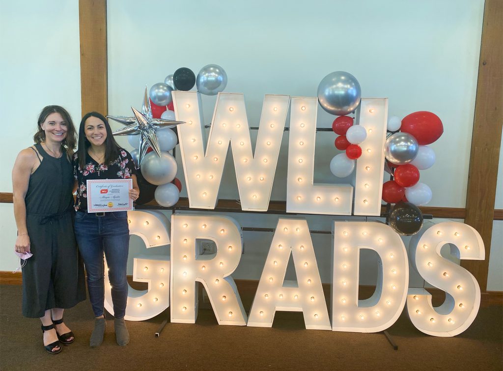 Amy Fulton and Morgan Aguilar pose by a large marquee sign reading, 'WLI Grads.'